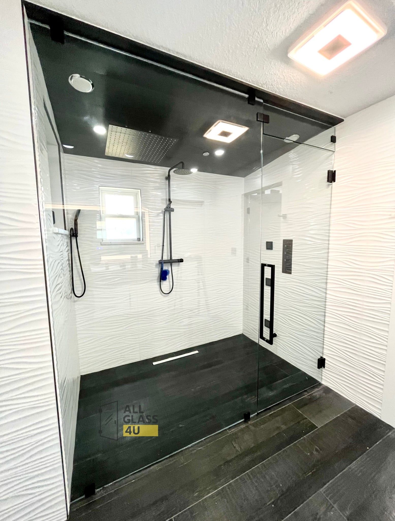 Frameless glass steam shower enclosure sealed to a dark ceiling, with matte black hardware