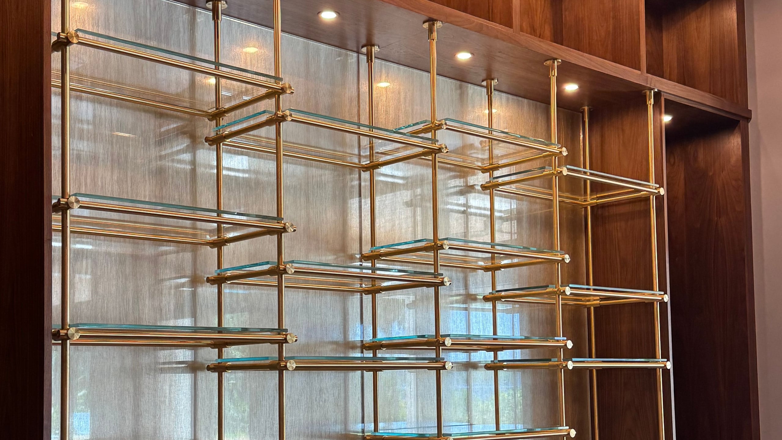 Floating glass shelves on brass posts in a walnut wall unit, installed by All Glass 4 U